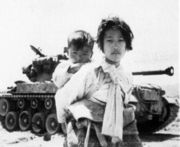 Mädchen trägt seinen Bruder an einem Panzer vorbei